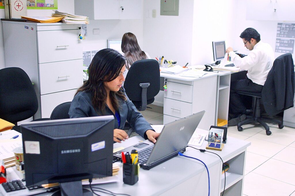 Trabajadores peruanos en una oficina realizando tareas administrativas frente a computadoras, en una jornada laboral de oficina.