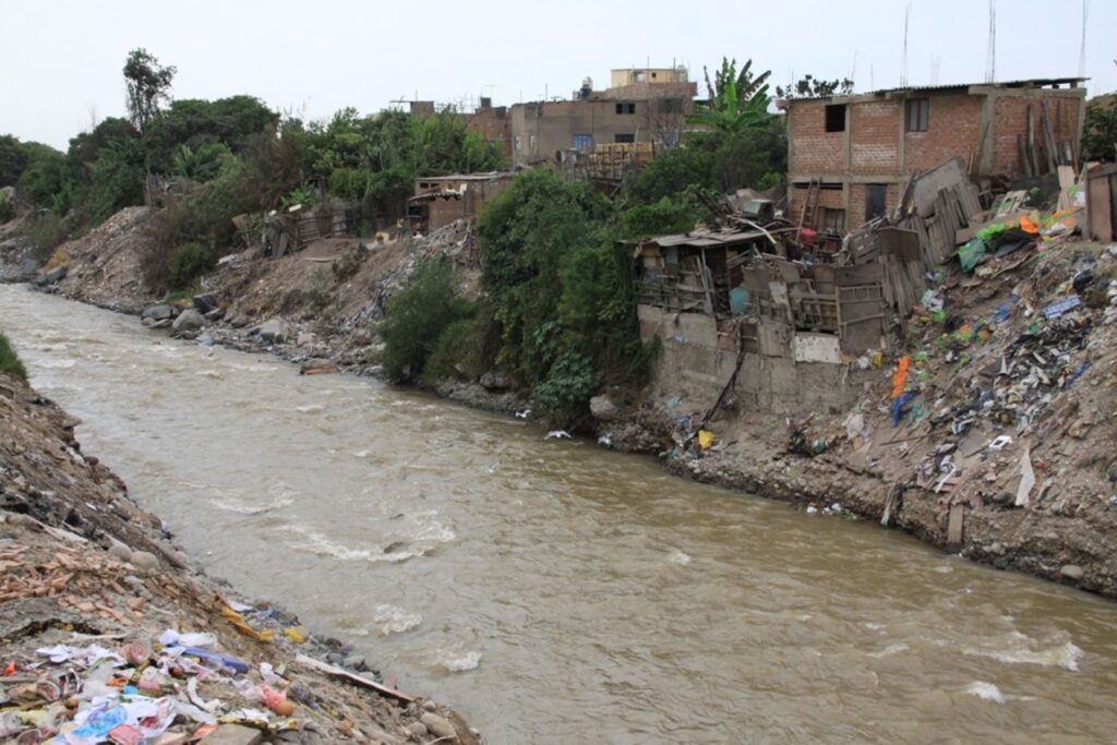 Viviendas precarias, acumulación de basura y desmonte en la ribera del río Rímac, reflejando el crecimiento urbano desordenado y la contaminación que afectan al principal río de Lima.