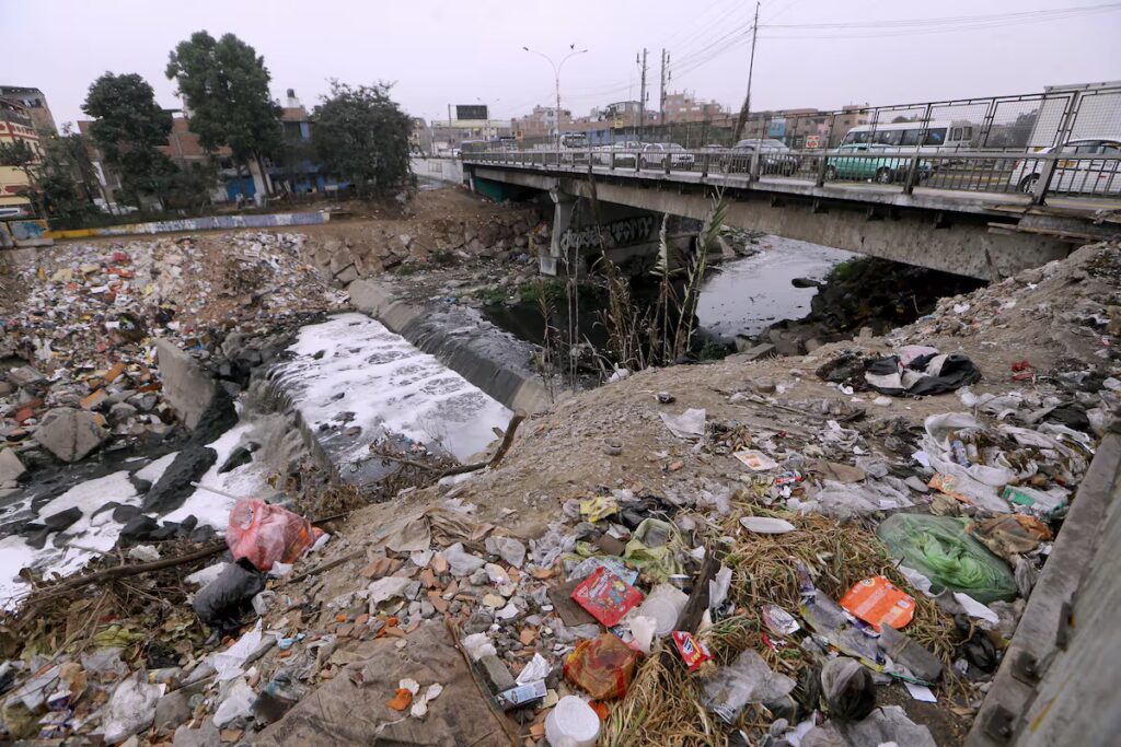 Contaminación por desechos sólidos y aguas residuales en el río Rímac. Botadero informal de basura en la ribera del río cerca de una zona habitada.