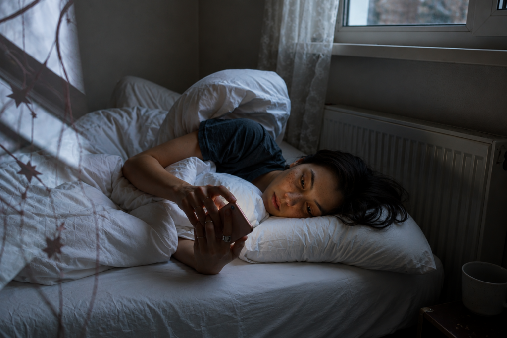 Joven acostada en su cama a oscuras usando el celular, con el rostro iluminado por la pantalla, ilustrando la adicción al scroll infinito y la dependencia digital.