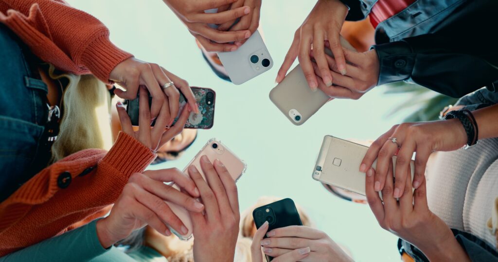 Grupo de amigos de la Generación Z conectados a sus celulares en círculo, ilustrando el uso de redes sociales y la comunicación digital.